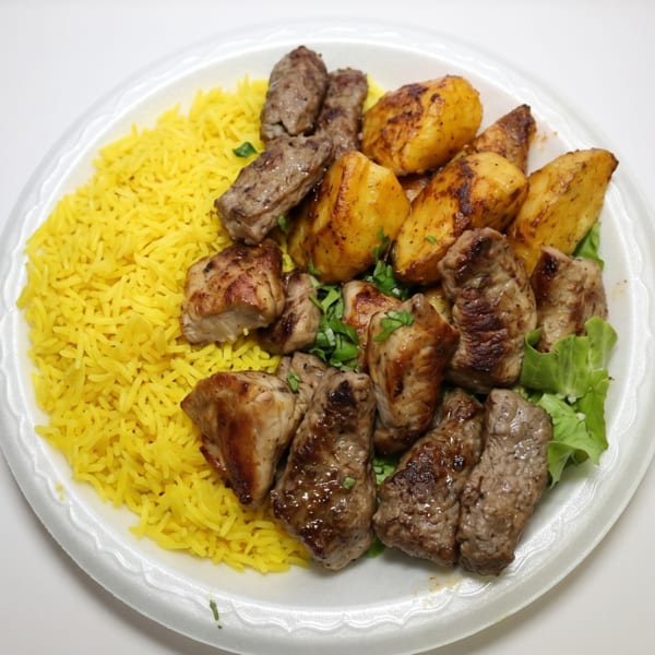 A white plate with yellow rice, roasted potatoes, and various grilled meats, garnished with parsley.