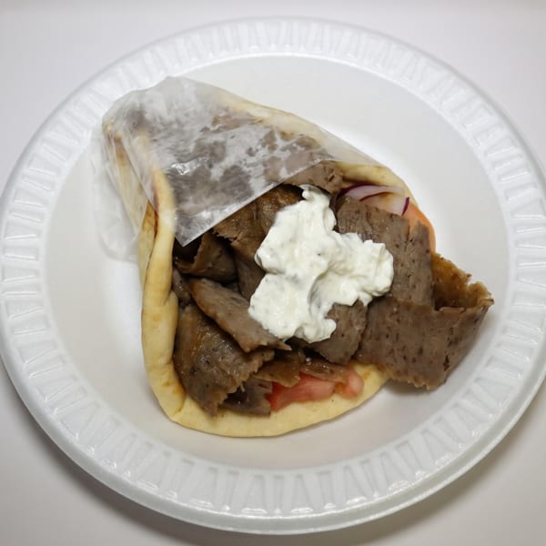 A gyro with meat, tomatoes, and tzatziki sauce on a white styrofoam plate.