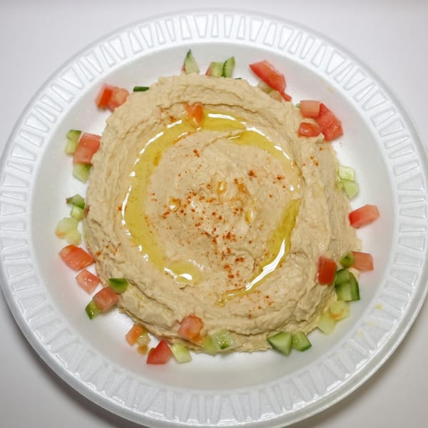 Creamy hummus drizzled with olive oil and sprinkled with paprika, garnished with diced tomatoes and cucumbers.