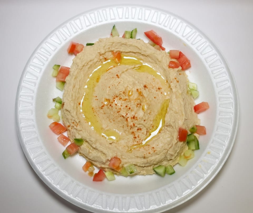Creamy hummus drizzled with olive oil and sprinkled with paprika, garnished with diced tomatoes and cucumbers.
