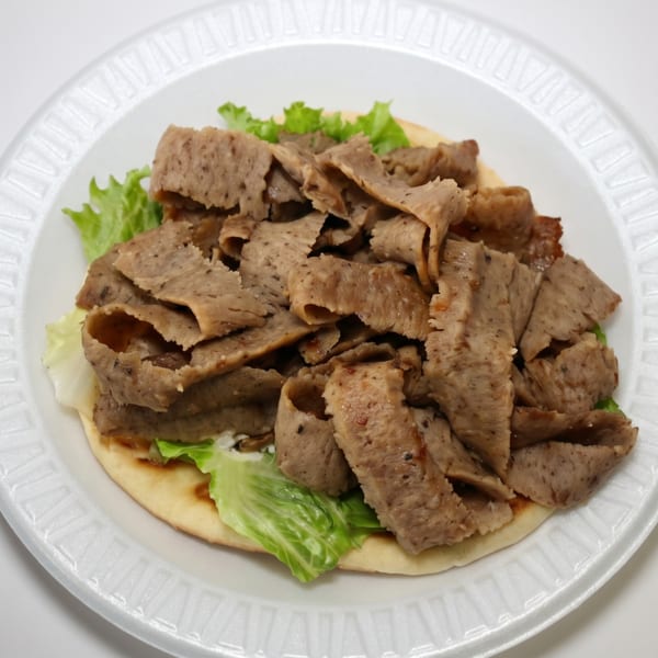 Gyro meat and lettuce on pita bread, served on a white disposable plate.