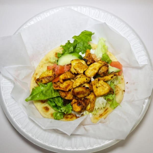 Chicken shawarma pita with lettuce, tomatoes, and cucumbers on a white plate.