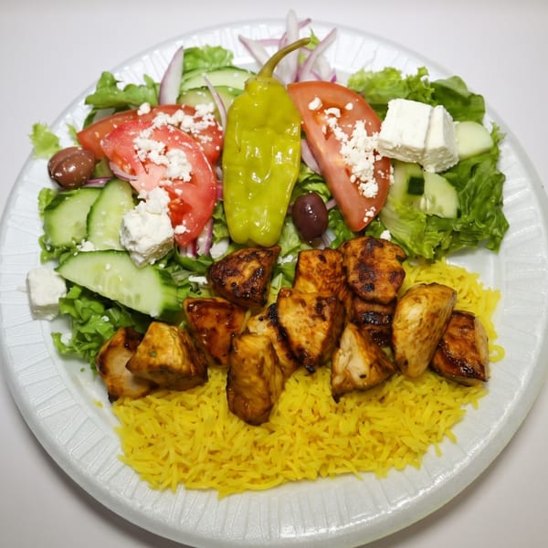 Chicken tikka with yellow rice, Greek salad, and a pepperoncini on a white plate.