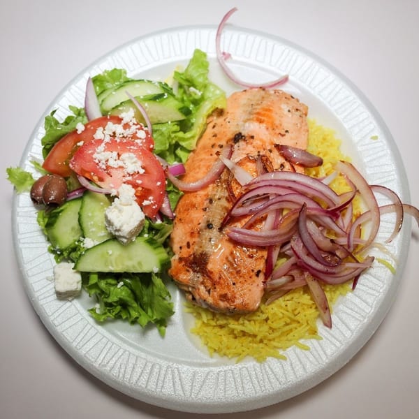 Grilled salmon with red onions, yellow rice, and a side salad with feta cheese and olives.